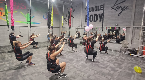 Group fitness class performing squats with suspension straps in a vibrant gym.